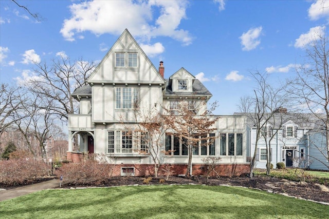 back of house featuring a chimney, a lawn, brick siding, and stucco siding