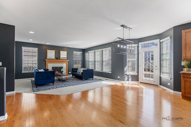 unfurnished living room with a notable chandelier, light wood-style flooring, recessed lighting, a lit fireplace, and baseboards