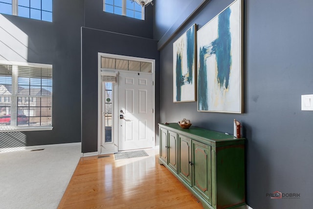 foyer featuring baseboards, a high ceiling, a healthy amount of sunlight, and light carpet