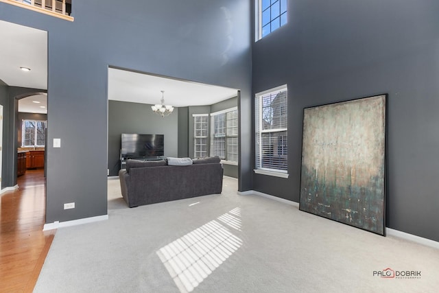 living area featuring arched walkways, a chandelier, baseboards, and a towering ceiling