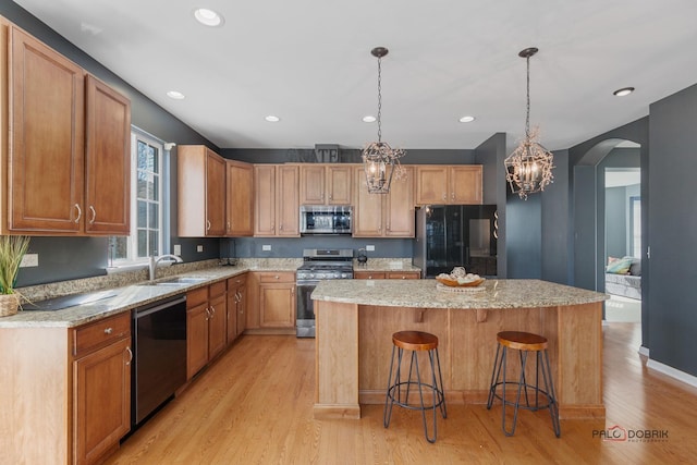 kitchen with light wood finished floors, a center island, arched walkways, stainless steel appliances, and a sink