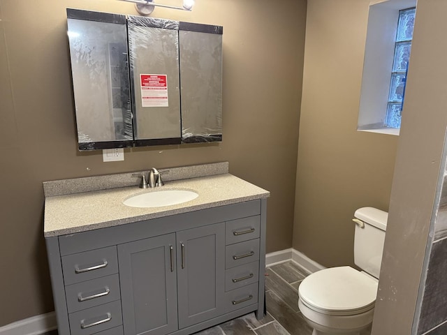 bathroom featuring vanity, toilet, baseboards, and wood tiled floor