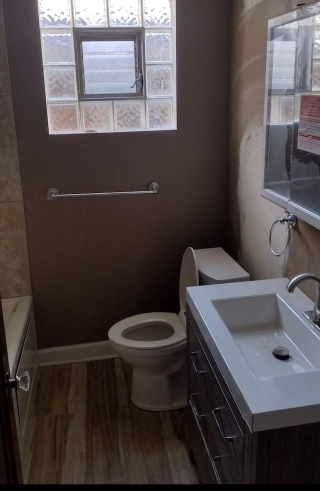 full bath featuring baseboards, toilet, a tub to relax in, and wood finished floors