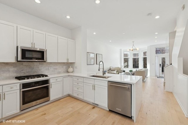 kitchen with a sink, backsplash, stainless steel appliances, a peninsula, and light countertops