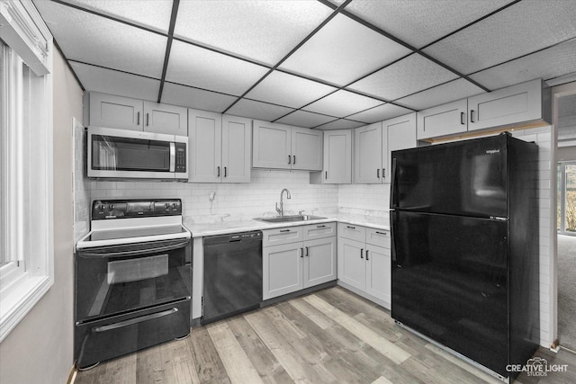 kitchen with backsplash, light countertops, light wood-style flooring, black appliances, and a sink