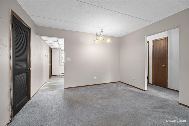 carpeted spare room with baseboard heating, baseboards, and an inviting chandelier