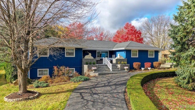 single story home with aphalt driveway, covered porch, and a front lawn