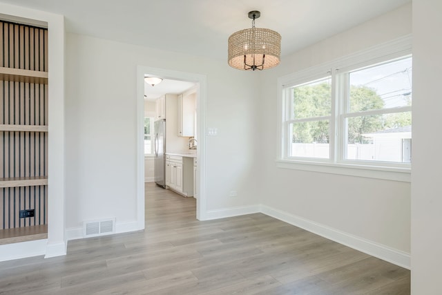 unfurnished dining area featuring a chandelier, light wood-type flooring, baseboards, and a sink