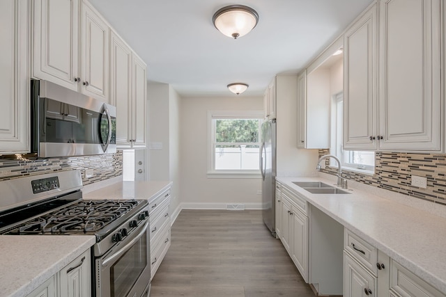 kitchen with stainless steel appliances, a sink, baseboards, light wood-style flooring, and tasteful backsplash