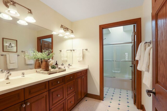 bathroom featuring double vanity, baseboards, bath / shower combo with glass door, and a sink