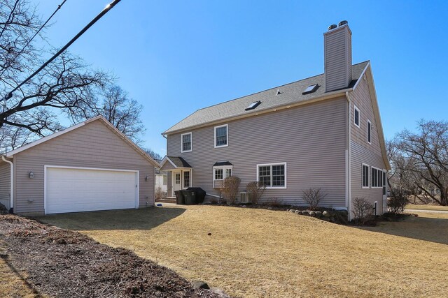 rear view of property with a shingled roof, a lawn, a chimney, a garage, and an outbuilding