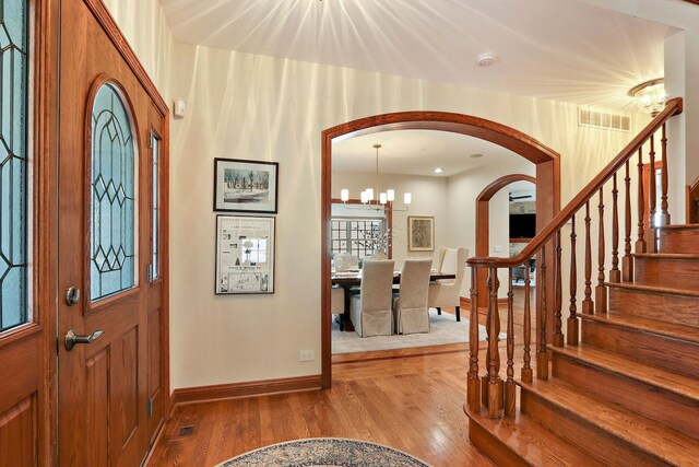 foyer featuring wood finished floors, visible vents, arched walkways, stairs, and a chandelier