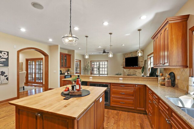 kitchen featuring tasteful backsplash, arched walkways, a peninsula, light wood finished floors, and wooden counters