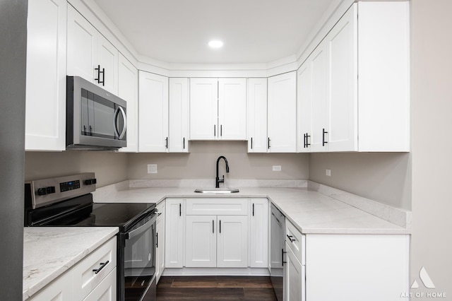 kitchen with light stone countertops, white cabinetry, stainless steel appliances, and a sink