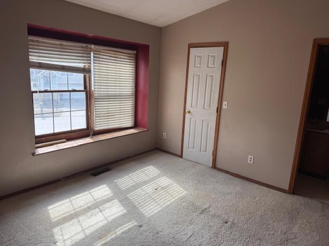 carpeted spare room featuring lofted ceiling, baseboards, and visible vents