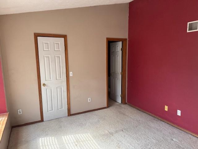 unfurnished bedroom with baseboards, visible vents, carpet floors, and lofted ceiling