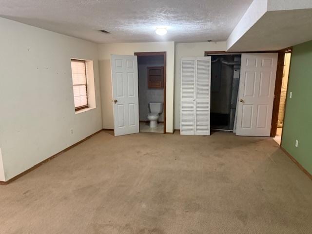 unfurnished bedroom with baseboards, light carpet, a textured ceiling, and connected bathroom