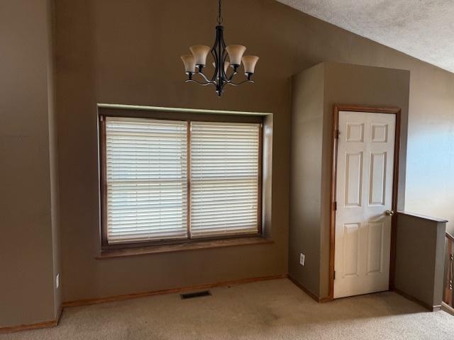 interior space featuring visible vents, light carpet, lofted ceiling, an inviting chandelier, and baseboards