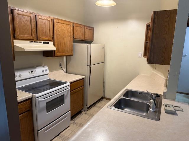 kitchen with under cabinet range hood, a sink, white appliances, light countertops, and light floors