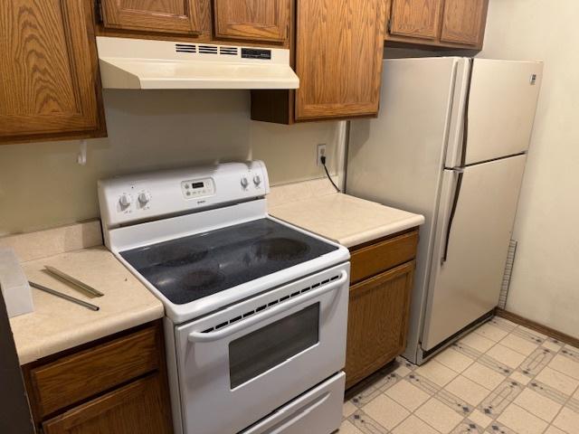 kitchen with white appliances, brown cabinetry, light floors, light countertops, and under cabinet range hood