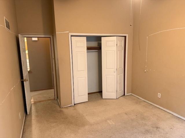 unfurnished bedroom featuring a towering ceiling, light colored carpet, visible vents, and a closet