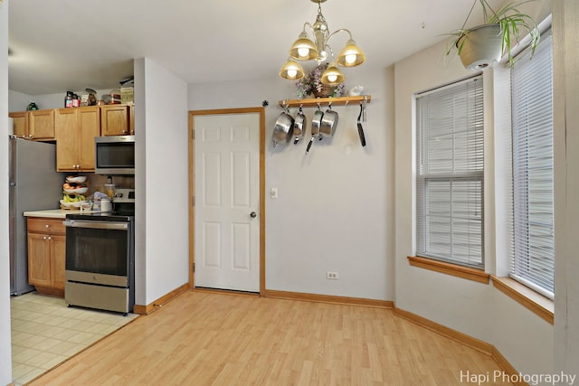 kitchen featuring light wood-type flooring, baseboards, stainless steel appliances, and an inviting chandelier