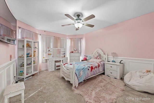 carpeted bedroom with ceiling fan, a decorative wall, and wainscoting