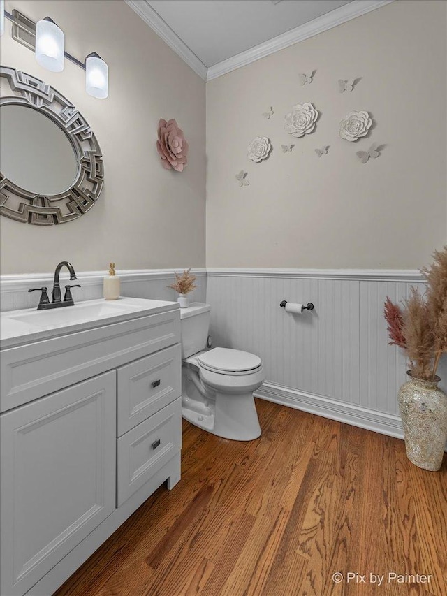 half bathroom featuring toilet, ornamental molding, wood finished floors, wainscoting, and vanity