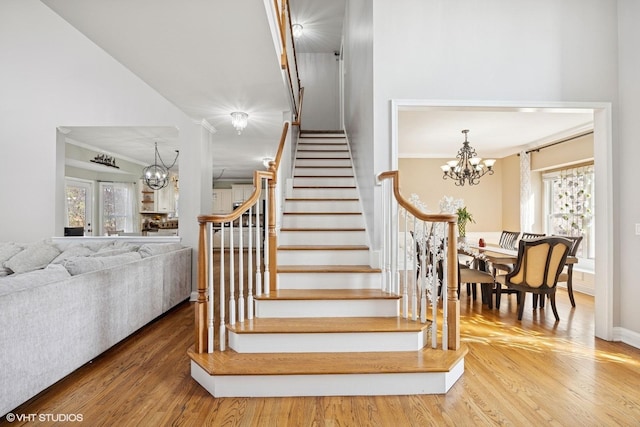 stairs with an inviting chandelier, crown molding, and wood finished floors