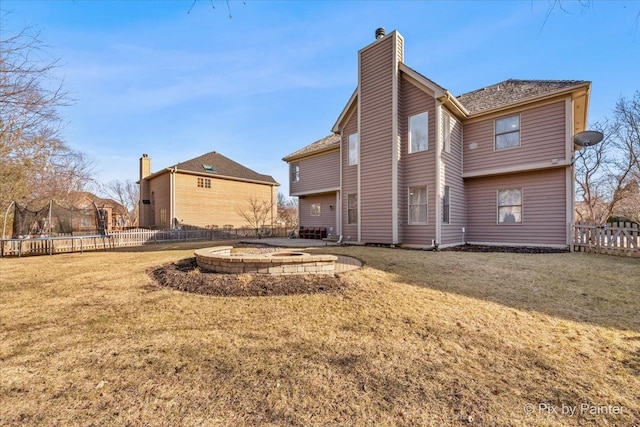 rear view of house featuring a trampoline, a lawn, a chimney, and fence