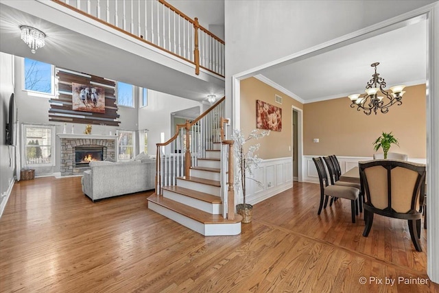 stairway with a stone fireplace, crown molding, a notable chandelier, and wood finished floors