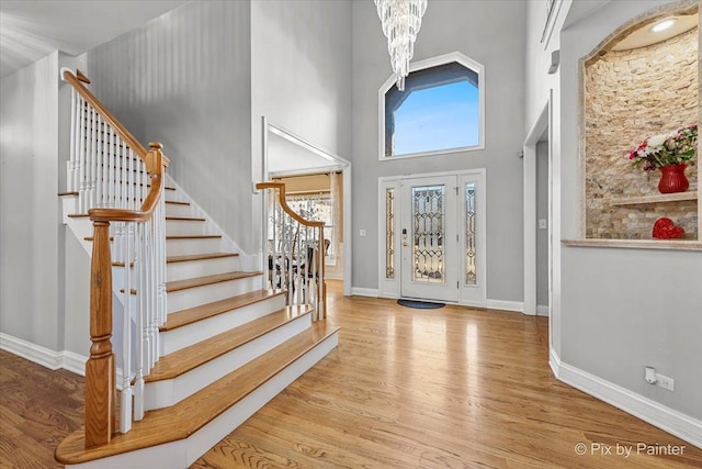 foyer entrance featuring baseboards, a chandelier, stairway, a high ceiling, and wood finished floors