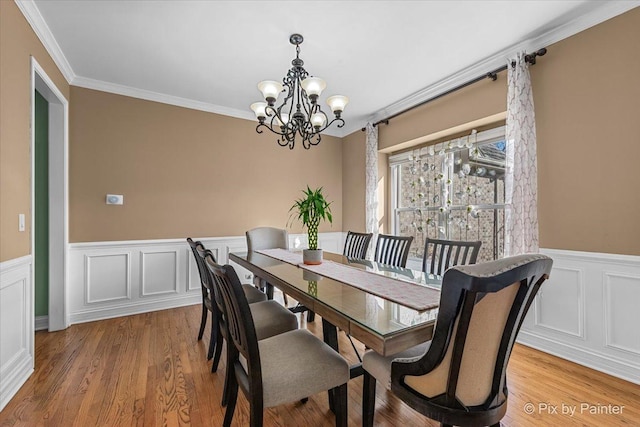 dining area with an inviting chandelier, light wood-style flooring, a wainscoted wall, and ornamental molding