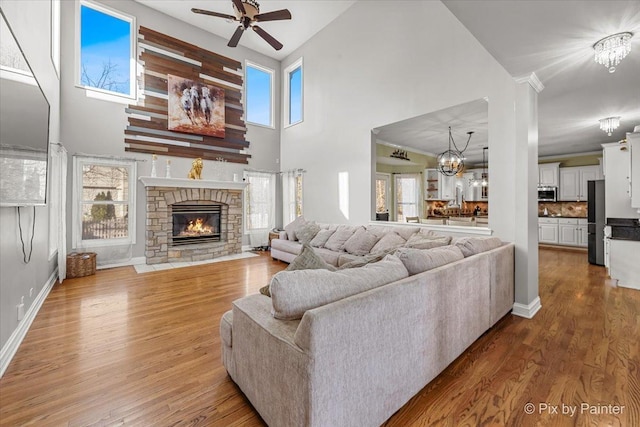 living area with wood finished floors, a fireplace, ornamental molding, a towering ceiling, and ceiling fan with notable chandelier