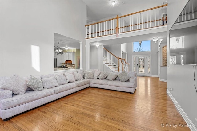 living area featuring stairs, a high ceiling, a notable chandelier, and light wood-type flooring