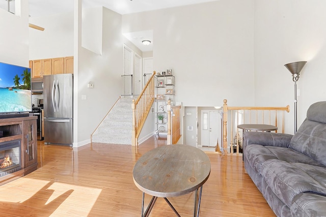 living area featuring light wood-type flooring, baseboards, and a towering ceiling