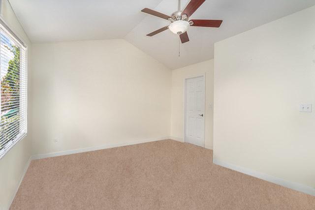 unfurnished room with lofted ceiling, a ceiling fan, baseboards, and light carpet