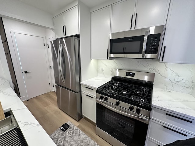 kitchen featuring light stone counters, white cabinetry, stainless steel appliances, and light wood-type flooring