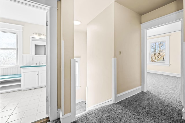 hallway featuring light colored carpet, baseboards, and a sink