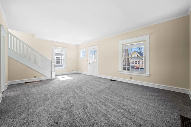 unfurnished living room featuring a wealth of natural light, carpet flooring, stairs, and visible vents