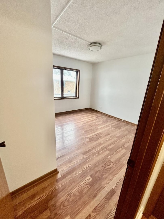 spare room with light wood-type flooring, baseboards, and a textured ceiling