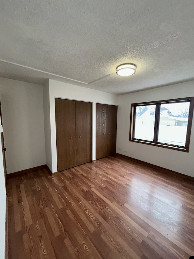 unfurnished bedroom featuring two closets, dark wood-style floors, and a textured ceiling