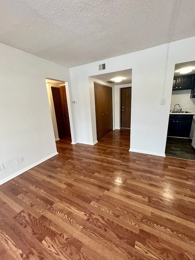 unfurnished living room with visible vents, baseboards, wood finished floors, a textured ceiling, and a sink