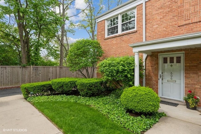 view of exterior entry featuring brick siding and fence