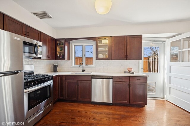 kitchen with visible vents, a sink, appliances with stainless steel finishes, light countertops, and glass insert cabinets