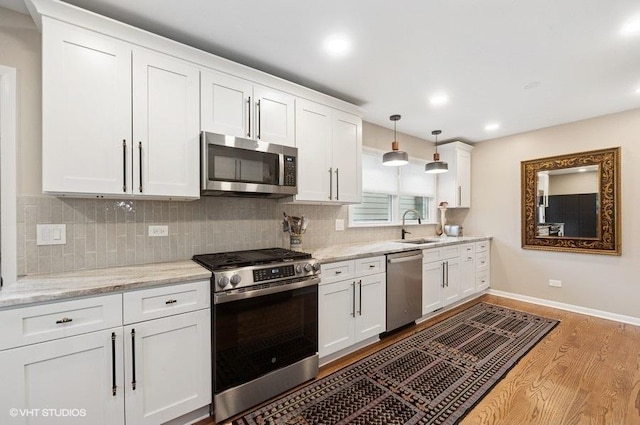 kitchen featuring a sink, tasteful backsplash, white cabinetry, appliances with stainless steel finishes, and wood finished floors