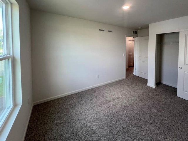 unfurnished bedroom with a closet, visible vents, dark carpet, and baseboards