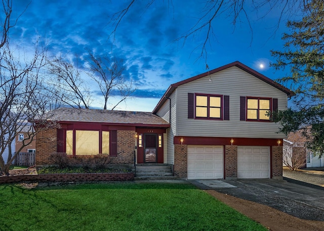 split level home with a front yard, a garage, brick siding, and driveway