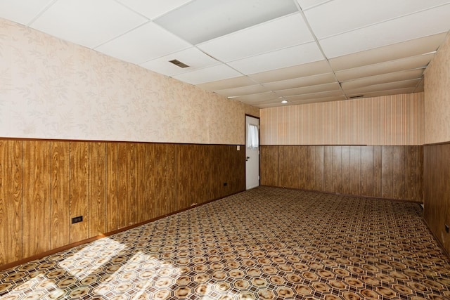 empty room featuring wooden walls, visible vents, a wainscoted wall, wallpapered walls, and a paneled ceiling