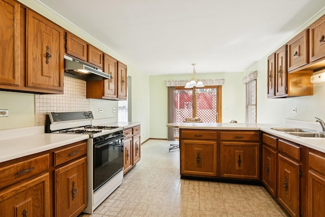 kitchen with under cabinet range hood, light countertops, a peninsula, gas stove, and a sink